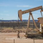 Industrial oil pumpjack in a desert setting under a clear blue sky, illustrating oil extraction technology.