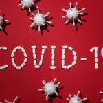 Creative depiction of COVID-19 using pills and virus models on a red backdrop.