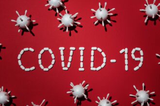 Creative depiction of COVID-19 using pills and virus models on a red backdrop.
