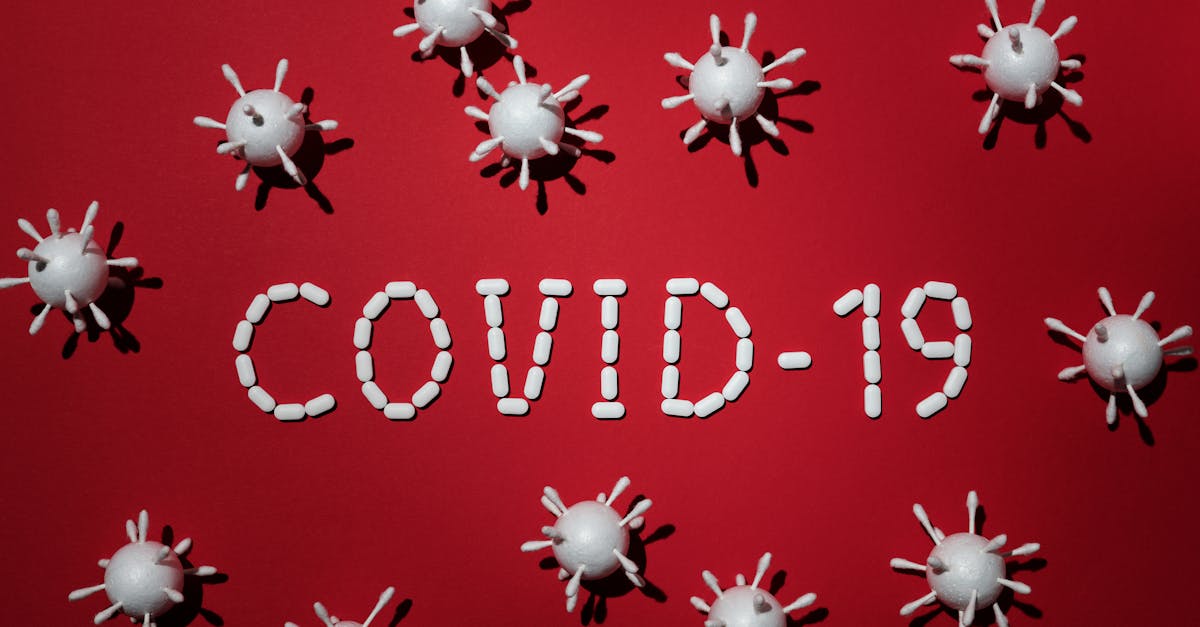 Creative depiction of COVID-19 using pills and virus models on a red backdrop.