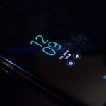 Close-up of a smartphone in the dark displaying digital clock and notifications.