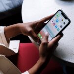 A person checks social media apps on a smartphone while sitting at a café table.