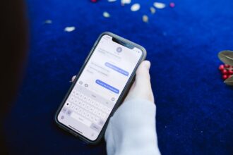 A person holding a smartphone displaying text messages on a blue surface with flowers.
