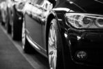 Close-up black and white image of a luxury car line-up focusing on vehicle headlights.
