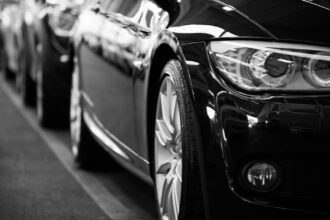 Close-up black and white image of a luxury car line-up focusing on vehicle headlights.