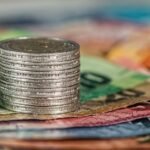 A stack of coins on top of various colored banknotes, symbolizing finance and currency.