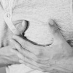 Black and white photo of a man clutching his chest, indicating discomfort or pain.