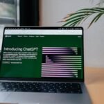 A laptop displaying ChatGPT on a desk by a window, featuring a modern home office setup.