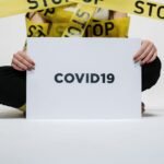 Person holding COVID-19 sign surrounded by yellow stop tape, symbolizing quarantine and safety.