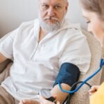 An elderly man having his blood pressure checked by a nurse during a routine health checkup indoors.