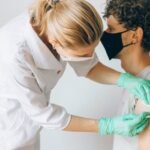 A healthcare worker gives a vaccine shot to a patient wearing a mask, highlighting medical safety and health precautions.