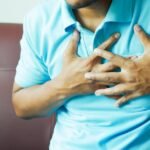 A close-up image of a man clutching his chest, indicating heart pain or discomfort.