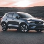A Volvo SUV parked on a scenic road at sunrise, surrounded by hills.