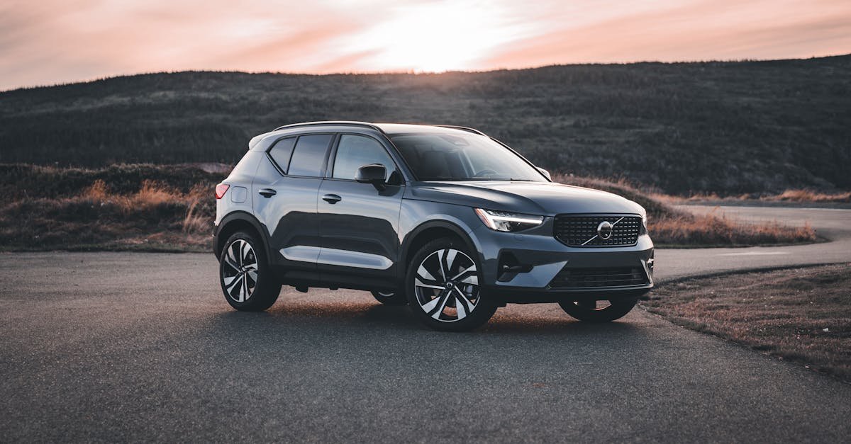 A Volvo SUV parked on a scenic road at sunrise, surrounded by hills.