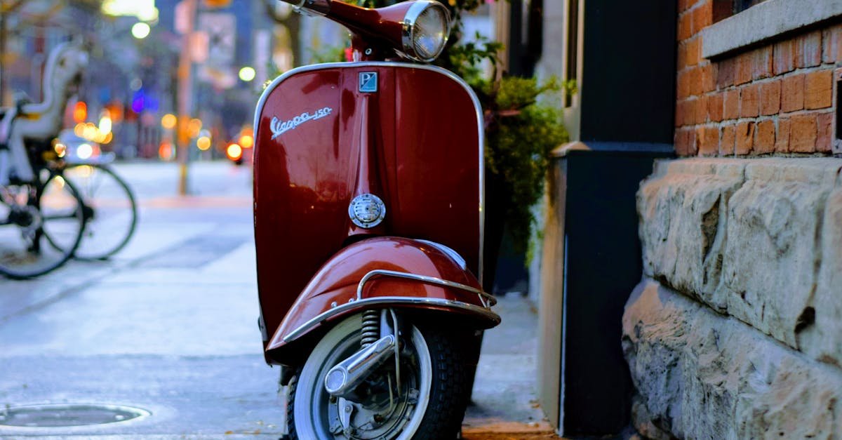 A classic red Vespa scooter parked beside a brick wall in an urban street setting.