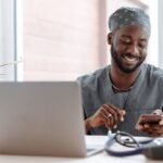 Smiling healthcare professional using phone in office with laptop and medical tools.