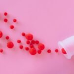 An artistic top-down view of a menstrual cup with red wool balls on a pink background.