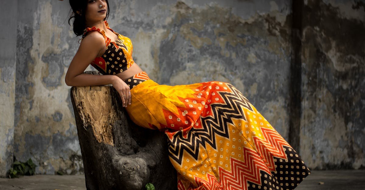 A woman elegantly poses on a tree stump wearing a colorful traditional outfit.