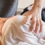 Crop anonymous medical specialist rubbing shoulders of male client lying on couch in medical salon