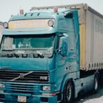 A blue Volvo truck parked outside a warehouse in an industrial area, daytime scene.