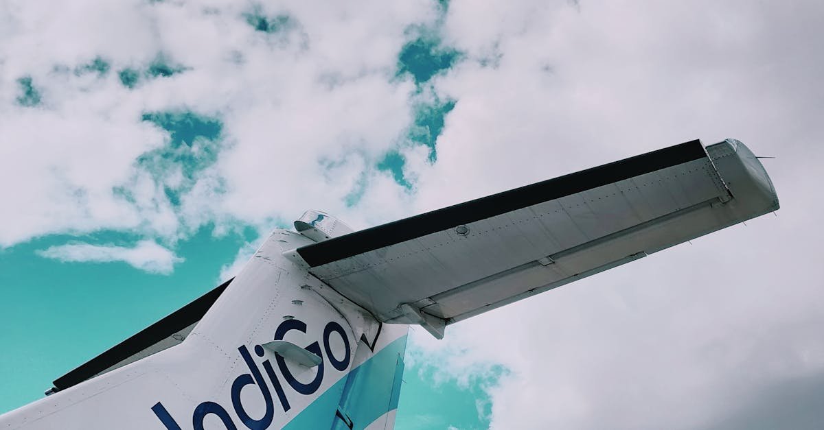 View of an airplane tail against a bright sky filled with clouds, showcasing travel themes.