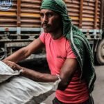 Indian worker in colorful attire loading sacks on a busy street, showcasing daily labor.