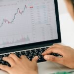 A woman working on financial analysis using a laptop with a stock market graph on screen.