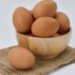 High resolution image of brown eggs in a wooden bowl placed on burlap fabric, ideal for food-themed content.