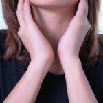 Close-up of a woman touching her neck, possibly indicating discomfort or throat pain.