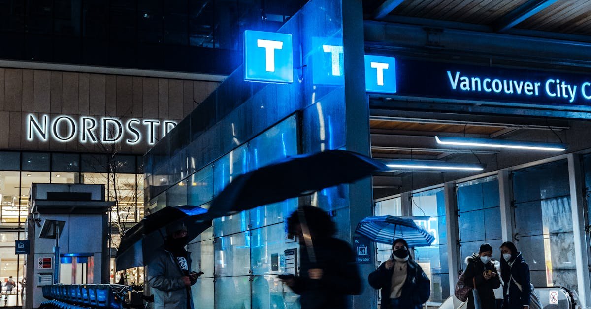 People walking with umbrellas at Vancouver City Centre Station during a rainy night.