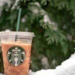 A refreshing iced beverage in a plastic cup set against a snowy evergreen backdrop.