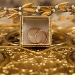 Close-up of gold wedding rings and a delicate tiara on an ornate golden background, symbolizing luxury and elegance.