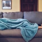 Person napping under a blue blanket on a comfortable couch in a modern living room setting.