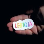 Hands holding a colorful LGBTQIA sign, symbolizing equality and support.