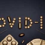 Creative COVID-19 concept with gold pills and syringes arranged on a dark background.