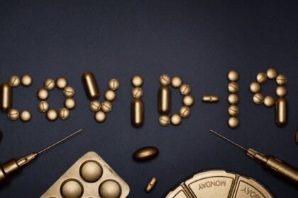 Creative COVID-19 concept with gold pills and syringes arranged on a dark background.