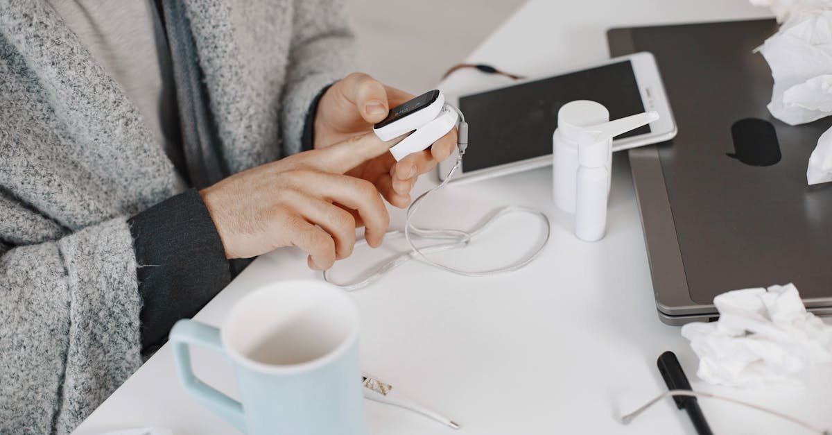 Adult using a pulse oximeter at a home desk, surrounded by tech and healthcare items.