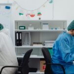 Two scientists in a lab, one examining a microscope, the other taking notes.