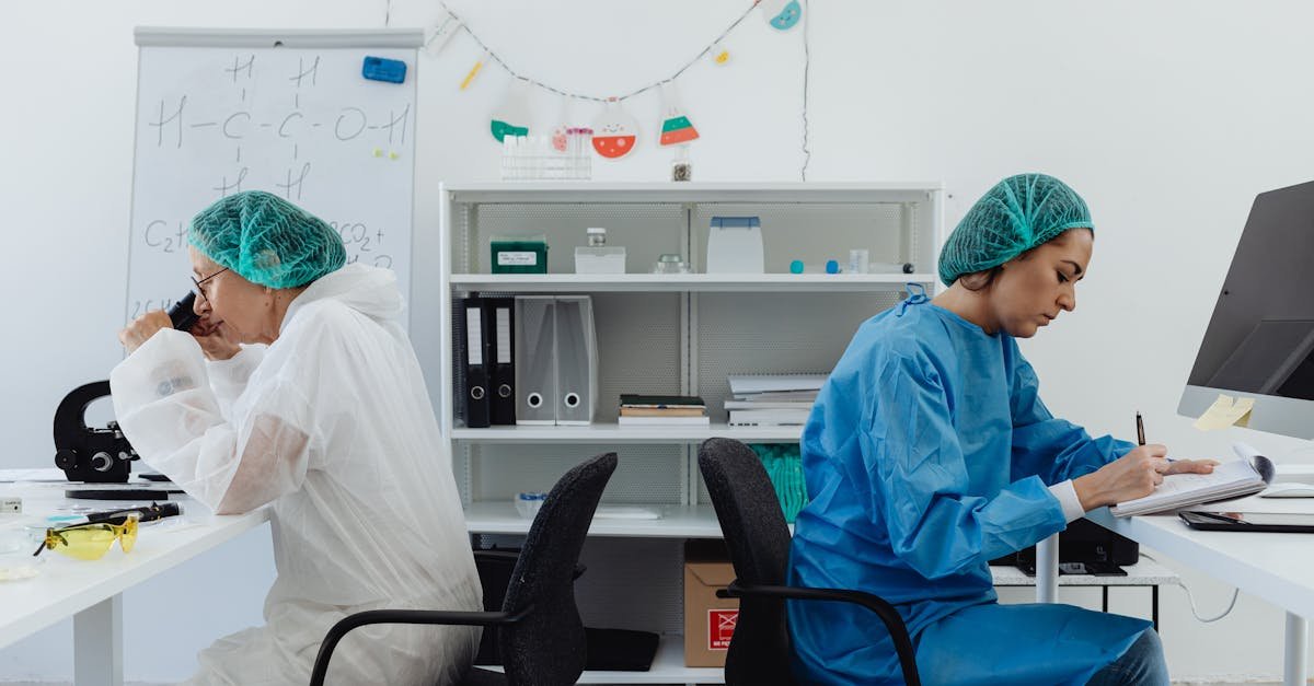 Two scientists in a lab, one examining a microscope, the other taking notes.