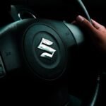 A hand grips the steering wheel of a Suzuki car, highlighting driving control.