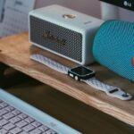 A close-up of a modern workspace featuring Bluetooth speakers, a smartwatch, and a keyboard.