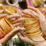 Vibrant close-up of hands displaying intricate golden bangles in a busy market setting.