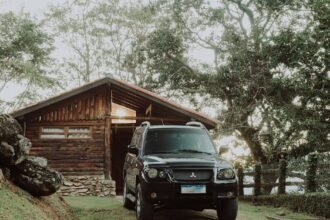 A black Mitsubishi SUV parked outside a wooden cabin surrounded by lush greenery.